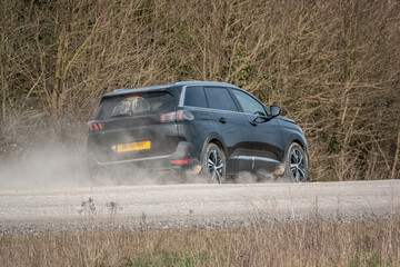 Obraz na płótnie Canvas Black Peugeot 5008 GT sport utility vehicle driving along an unmade stone track road thowing up dust