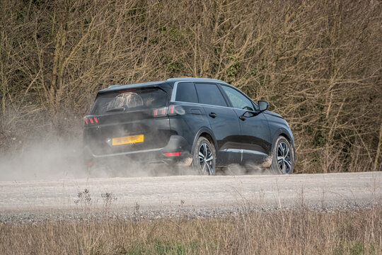 Black Peugeot 5008 GT sport utility vehicle driving along an unmade stone track road thowing up dust