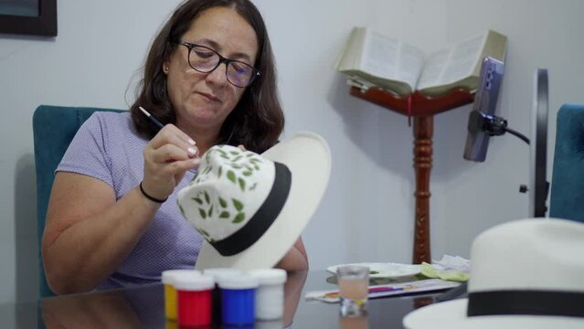 middle aged latina woman making a handicraft, painting a hat. 4k video