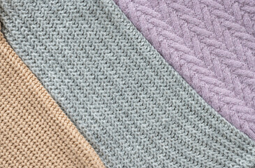 A bunch of knitted sweaters in warm pastel colors with different knitting patterns, the texture is clearly visible. Stylish knitwear for the autumn-winter season. Close up, copy space for text.