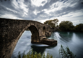 Fototapeta na wymiar Stone arch bridge over river in Arta city, Greece.