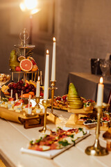 in backyard of villa in Tuscany there is banquet wooden table decorated with cotton and eucalyptus compositions, glasses, burning candles and plates are placed on table, evening.