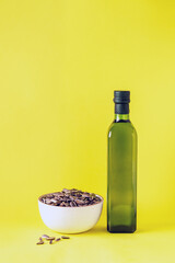 glass bottle with oil and a cup with seeds on a yellow background