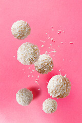 round candies in coconut flakes fly on a pink background