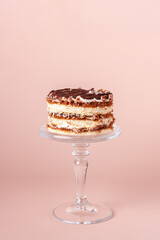 round tiramisu on a glass stand on a beige background, close-up