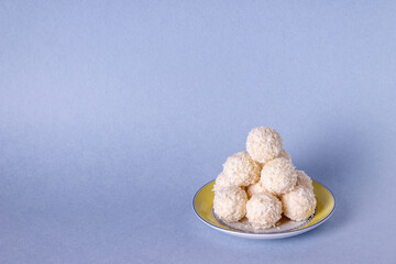round candies in coconut flakes on a blue background, copy space