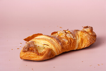 croissant with marzipan, sprinkled with almonds, on a pink background, close-up