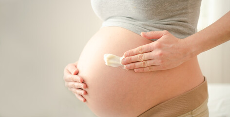 Close up of pregnant woman applying moisturizing cream on her belly. Health care and medicine...