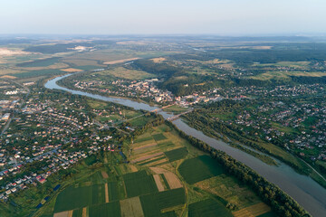 Aerial landscape view of village houses and distant green cultivated agricultural fields with growing crops on bright summer day
