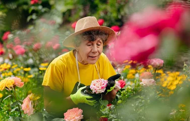 Foto op Canvas Senior woman gardener in a hat working in her yard and trimming flowers with secateurs. The concept of gardening, growing and caring for flowers and plants. © bondvit