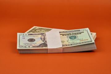 Two bundles of dollar bills on an orange table.