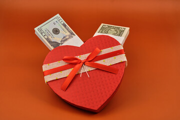 Gift in the shape of a heart full of dollars with an orange background.