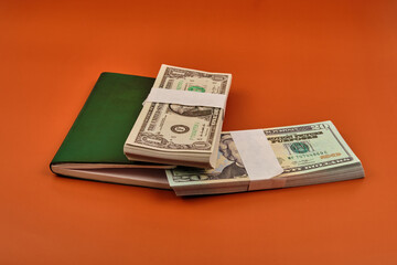 Green colored notebook with two bundles of dollars on an orange table.