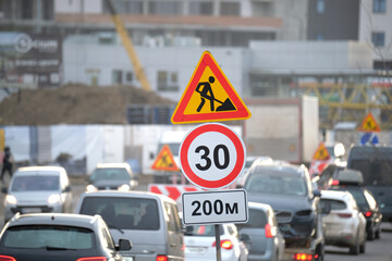 Roadworks warning traffic signs of construction work on city street and slowly moving cars