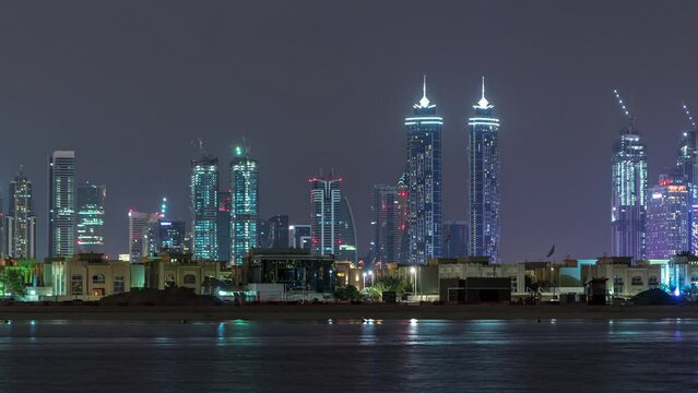 Modern Dubai city skyline timelapse at night with illuminated skyscrapers over water surface