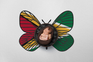 Tiny baby portrait with wings in color of national flag. Newborn photography concept. Guyana