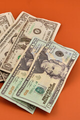 Dollar bills lying on an orange table. Photography in vertical format.