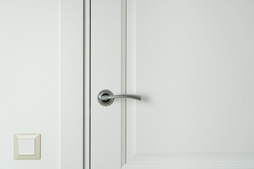 Closed white wooden interior door with handle and light switch on the wall.
