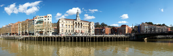 Naklejka na ściany i meble Panoramic view of the river in the city of Bilbao on a day with a blue sky and some white clouds. Bilbao, Spain, 03-27-2022