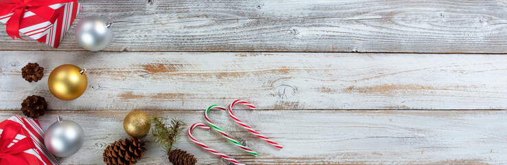 Traditional silver and gold Christmas balls with presents, candy canes and pine cones on white wood