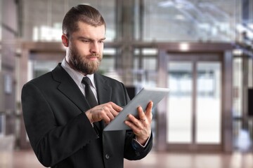 Thoughtful Businessman in a Suit Using digital tablet while Standing in Office