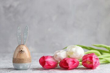 Festive Easter composition with tulips and Easter bunny against grey wall. Holiday greeting card. Copy space for text, selective focus