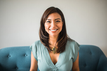portrait of a smiling latin woman looking at the camera sitting on the sofa at home