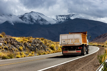 Truck drives on asphalt road with snowy hills in the background in Las Cuevas, Salta, Argentina