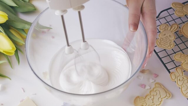 Cropped shot of woman using mixer machine making cookie icing for decoration. Woman holding glass bowl with sugar glaze and electric mixer. Easter holiday backing. Static shot. 4K UHD