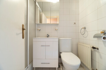 Toilet with white wooden cabinet, cabinet with mirror doors, sink, white tiles and fine aluminum radiator