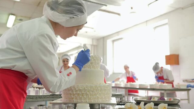Production of confectionery products. A woman in gloves decorating a cake.Production at the factory of chocolate, sweets or cakes. Food industry. Confectionery products.Confectionery factory or bakery