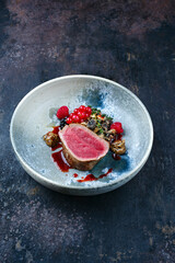 Modern style traditional fried dry aged angus beef filet medaillons natural with mushroom tartar, truffle cream and forest berries served as close-up on a design bowl