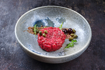 Modern style gourmet tartar raw from beef filet with capers and amarena cherry served with truffle cream and lettuce as close-up on a Nordic design plate
