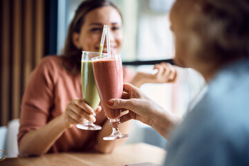 Close-up of mother and daughter toast with drinks in cafe.