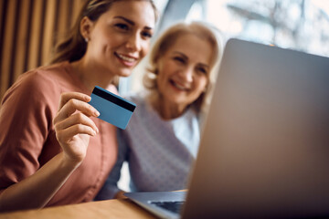 Close-up of mother and daughter shopping online while using laptop and credit card.