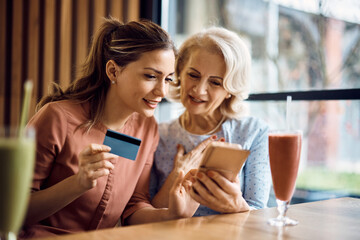 Mid adult woman and her senior mother e-banking over smart phone in cafe.