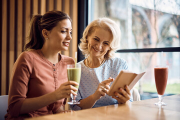 Happy senior woman and her adult daughter using smart phone in cafe.