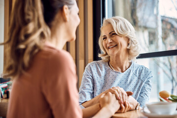 Happy senior woman enjoys in conversation with her adult daughter in cafe.