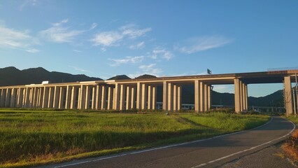 Fototapeta na wymiar 田畑の中にある夕日に照らされる高架高速道路と青空その奥には新幹線