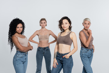 Brunette woman in top posing near interracial friends isolated on grey, feminism concept.