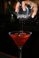 bartender pouring a cosmopolitan into a chilled martini glass