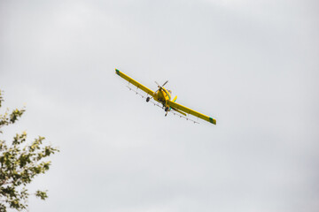 The underside of a yellow crop dusting sptay plane flying in the air