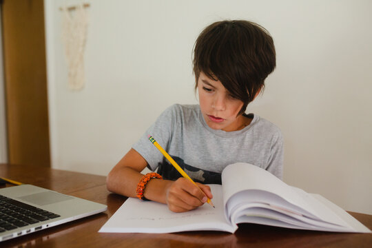 Boy attending homeschooling class through laptop at table in living room
