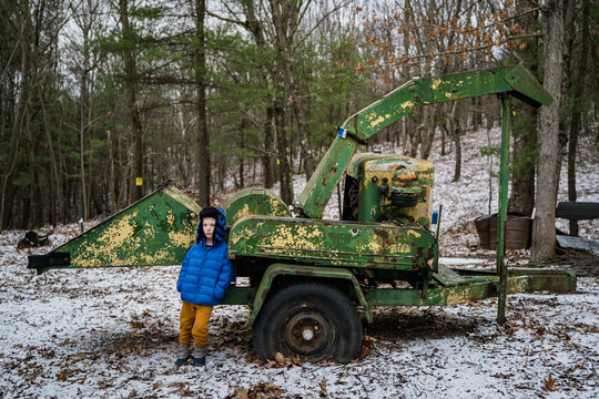 A little boy stands next to an old wood chipper.