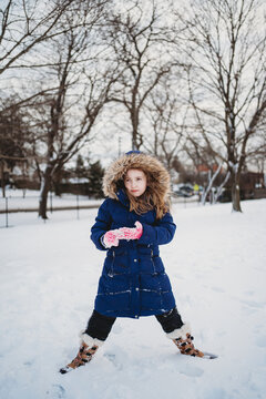 A girl wearing a large fur hood stands in the snow.