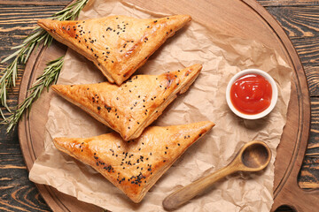 Board with tasty Uzbek samsa and tomato sauce on wooden background