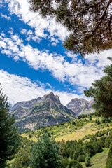 Obraz premium a mountain range framed with vegetation at the edges, on a summer day with a sky with cottony clouds, Pena Telera, Valle de Tena, Biescas, Huesca, Spain