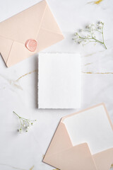 Wedding paper card, pink envelopes, gypsophila branches on marble desk. Elegant wedding stationery set. Flat lay, top view, copy space.