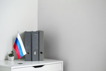 Chest of drawers with folders, houseplant and Russian flag near light wall