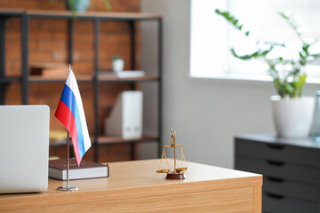 Russian flag, book, judge scales and laptop on table in office